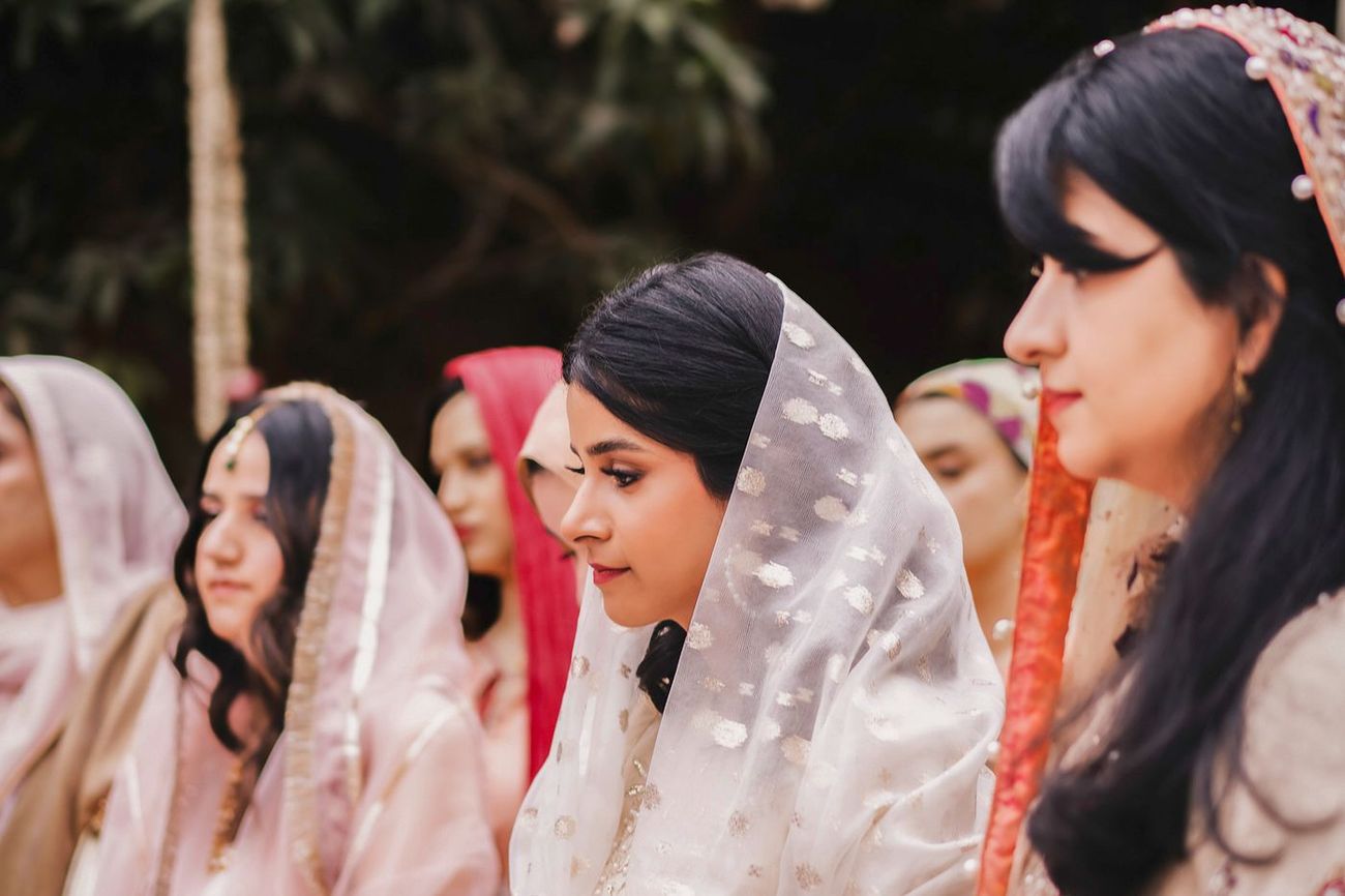 Group of female guests in profile, heads covered with dupattas, watching the ceremony