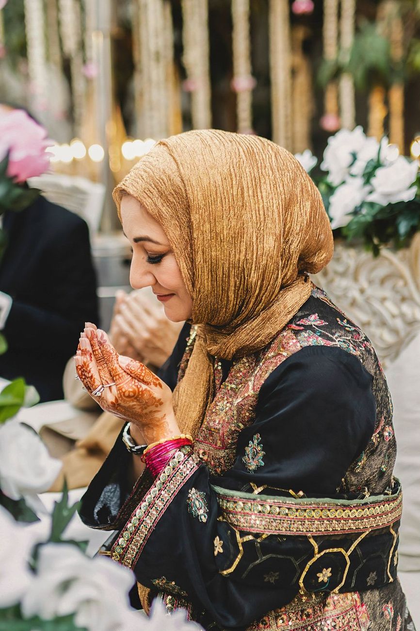 Groom's mother in a dua pose, hands cupped, henna visible on her hands
