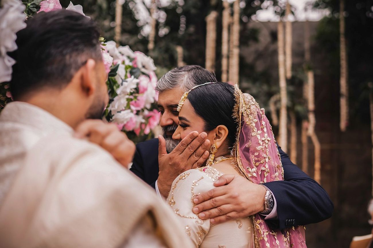 Tender moment of the bride's father cupping her face, groom looking on