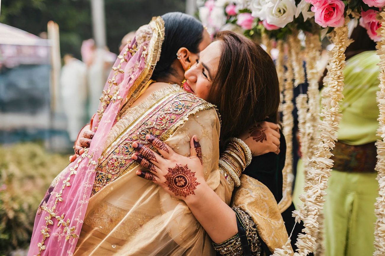 Bride hugging another woman warmly, henna visible on both their hands
