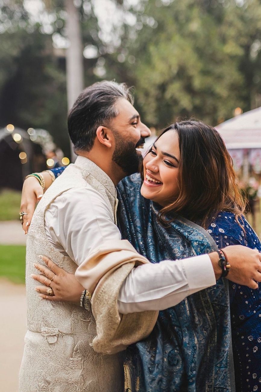 Groom hugging a female guest, joyful laughter, outdoor garden setting