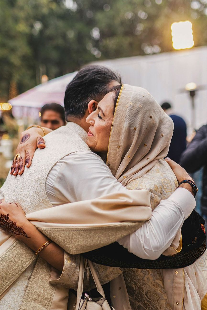 Groom hugging an older woman in a beige embroidered headscarf