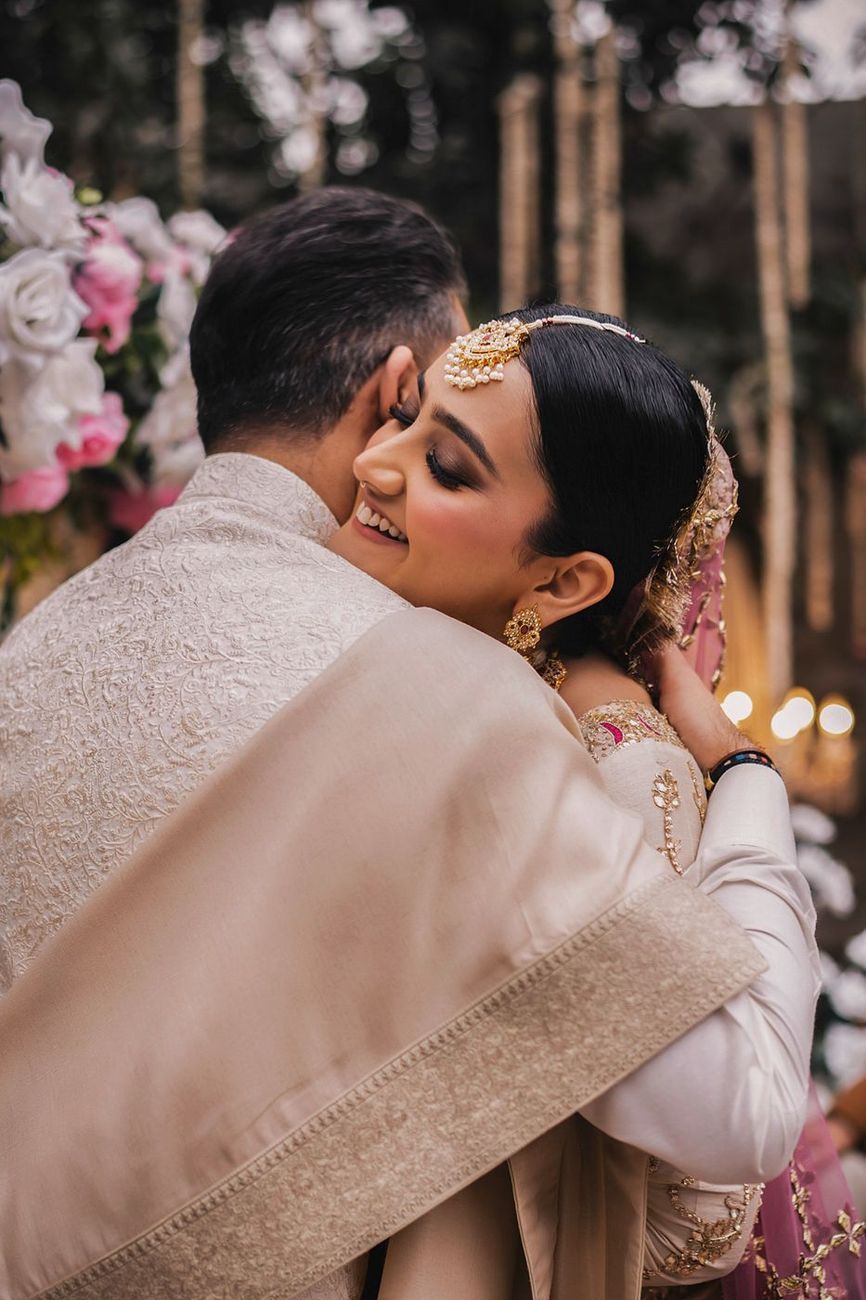 Bride and groom embracing tenderly, laughing, string lights blurred behind