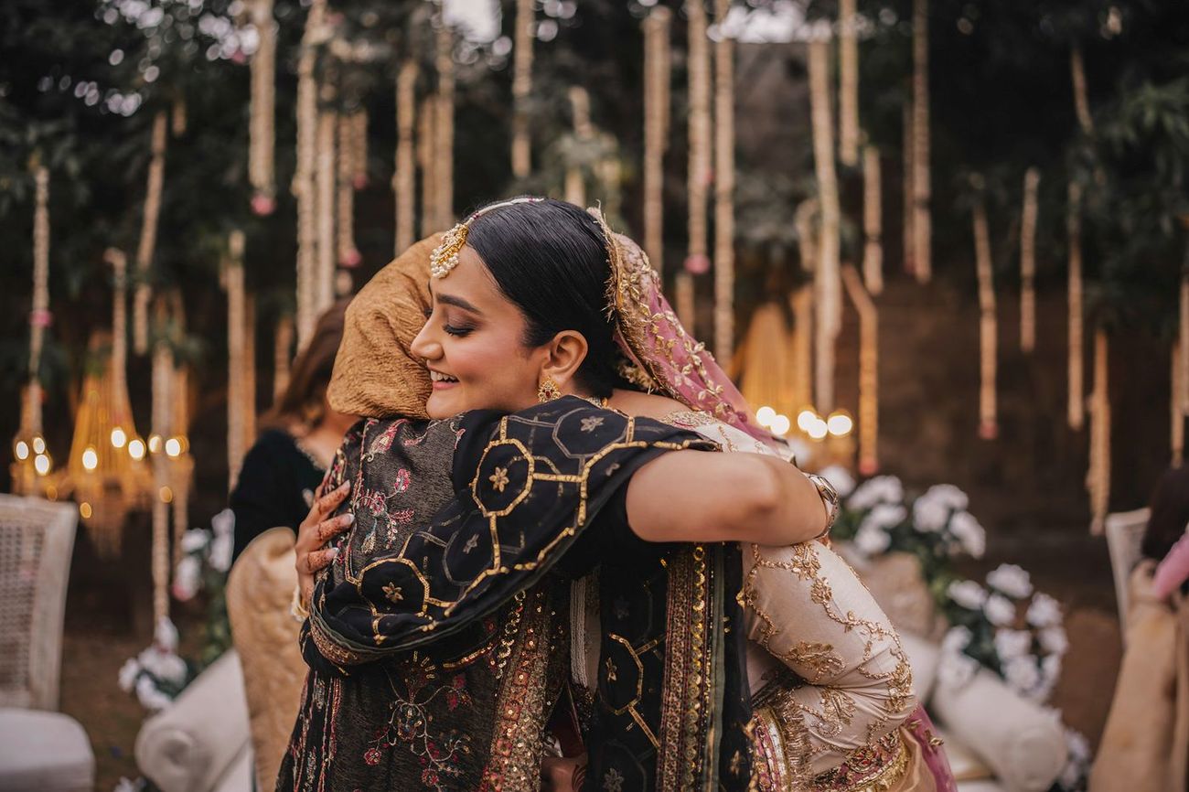 Bride hugging the groom's mother, candle-lit garland backdrop