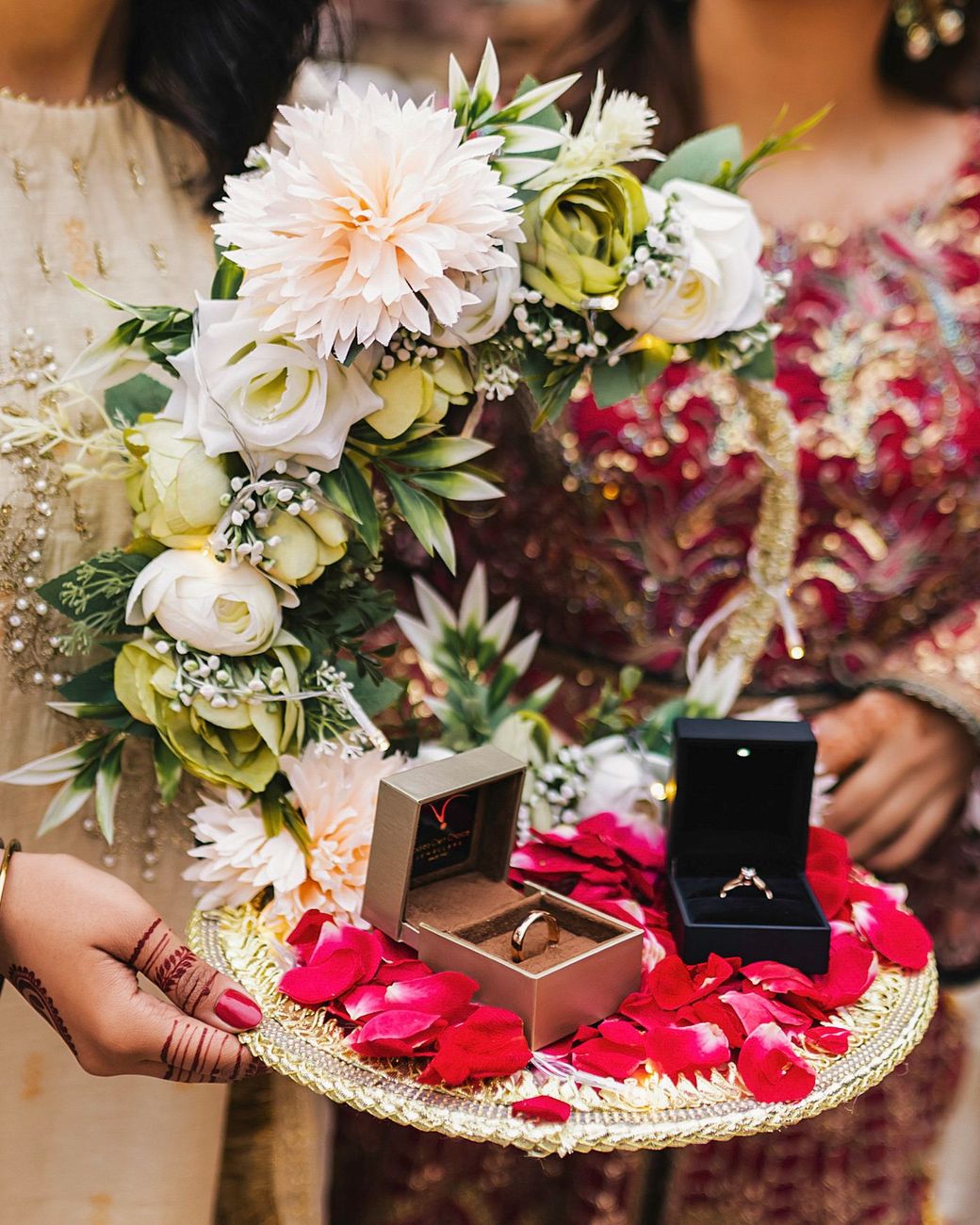 Close-up of the wedding ring boxes presented on a flower-decorated tray with red rose petals