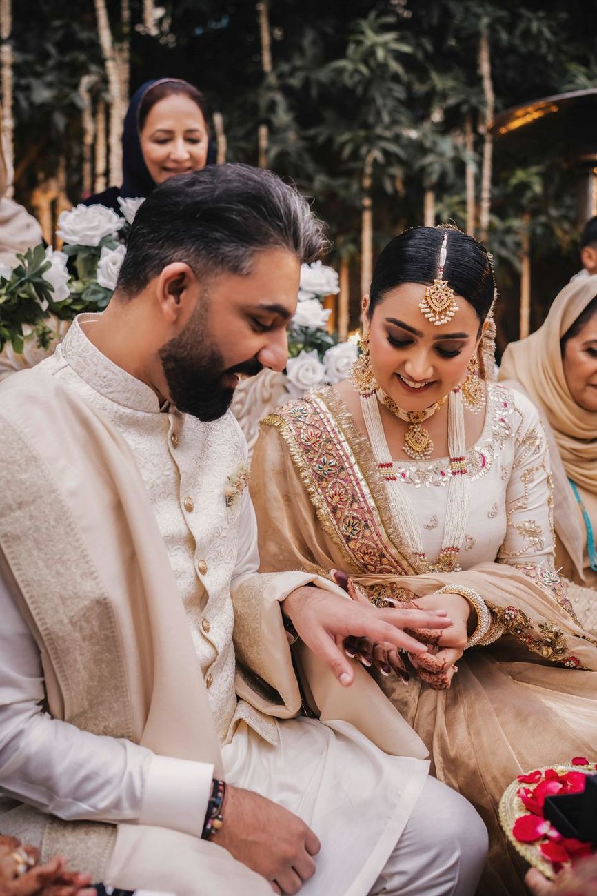 Bride sliding the ring onto the groom's hand during the ring exchange, both smiling