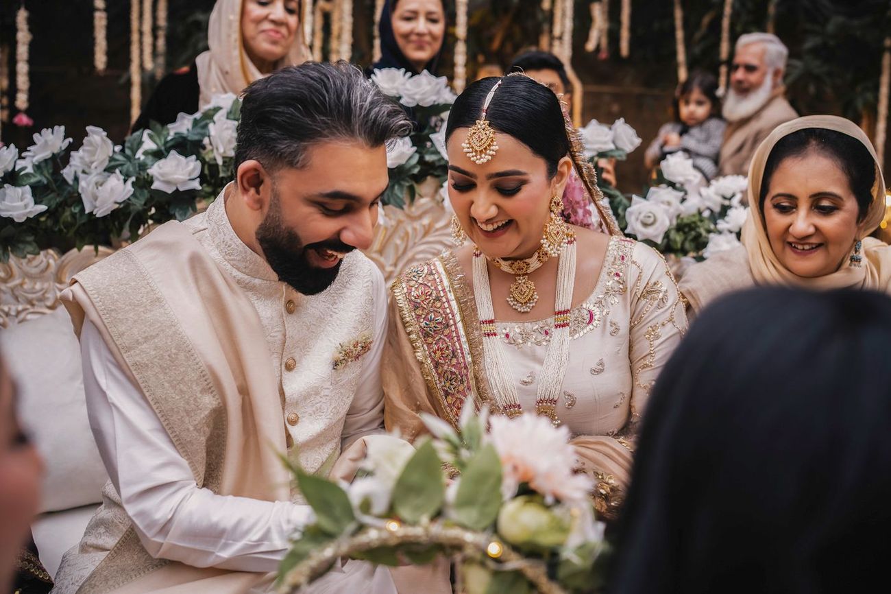 Couple laughing together with the ring tray held up in front of them, family seated around