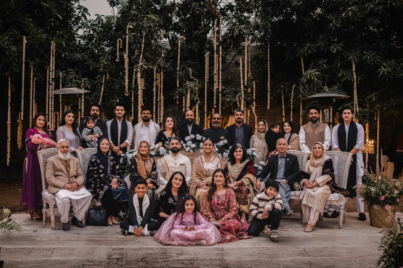 Even larger extended family group photo, three rows deep, with hanging garlands and a chandelier behind