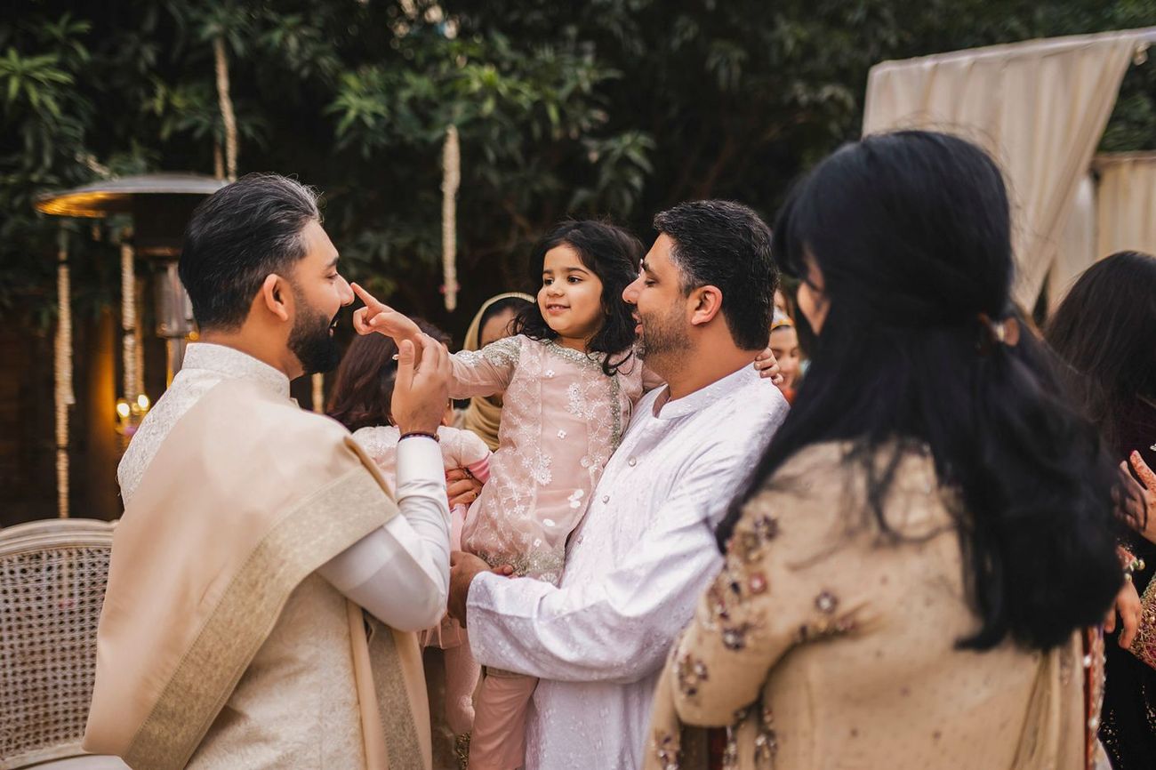Playful candid moment of a man holding a young girl reaching toward the groom's face