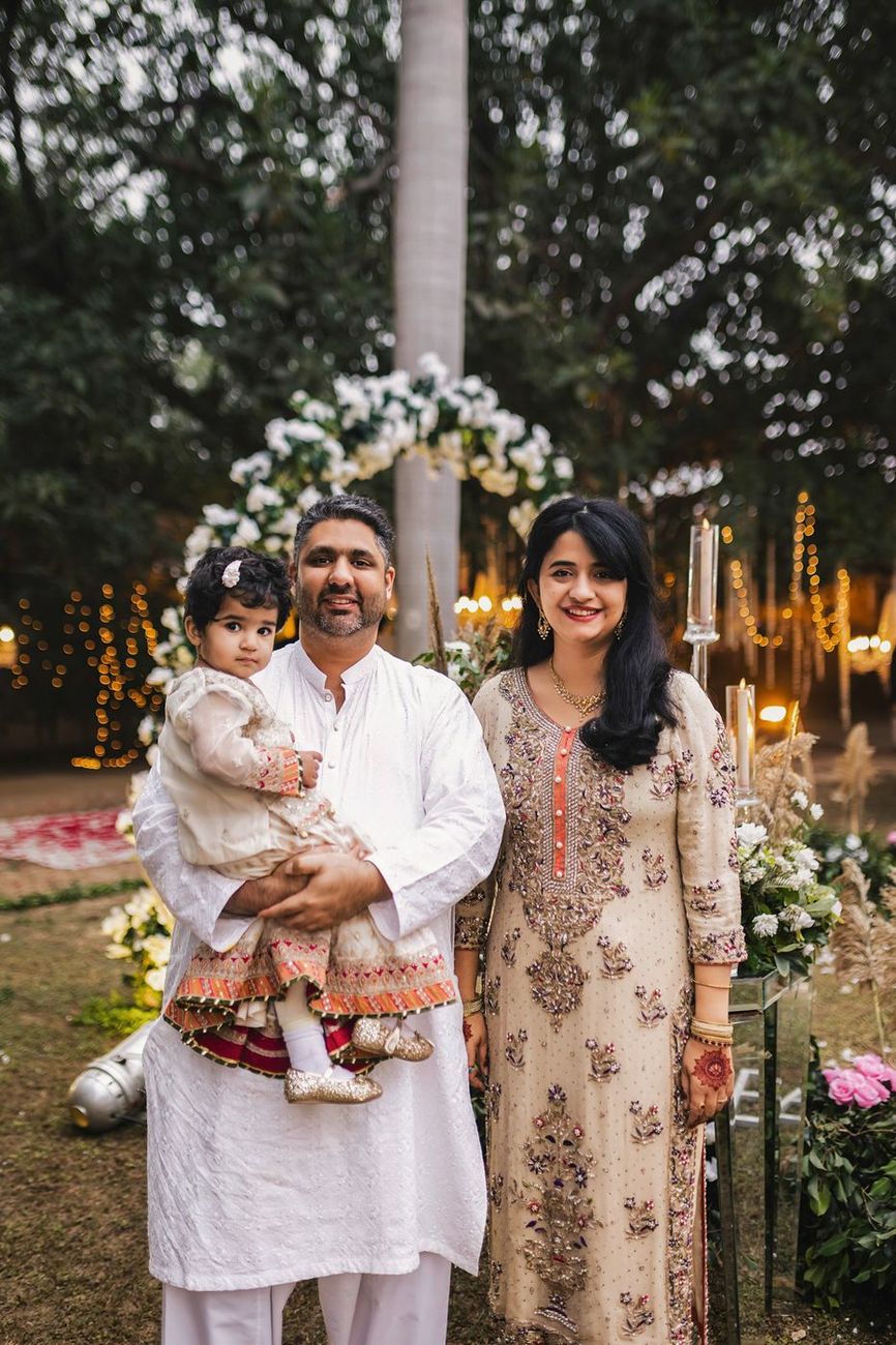 Guest family portrait, a man holding a toddler, standing beside a woman near a small floral arch