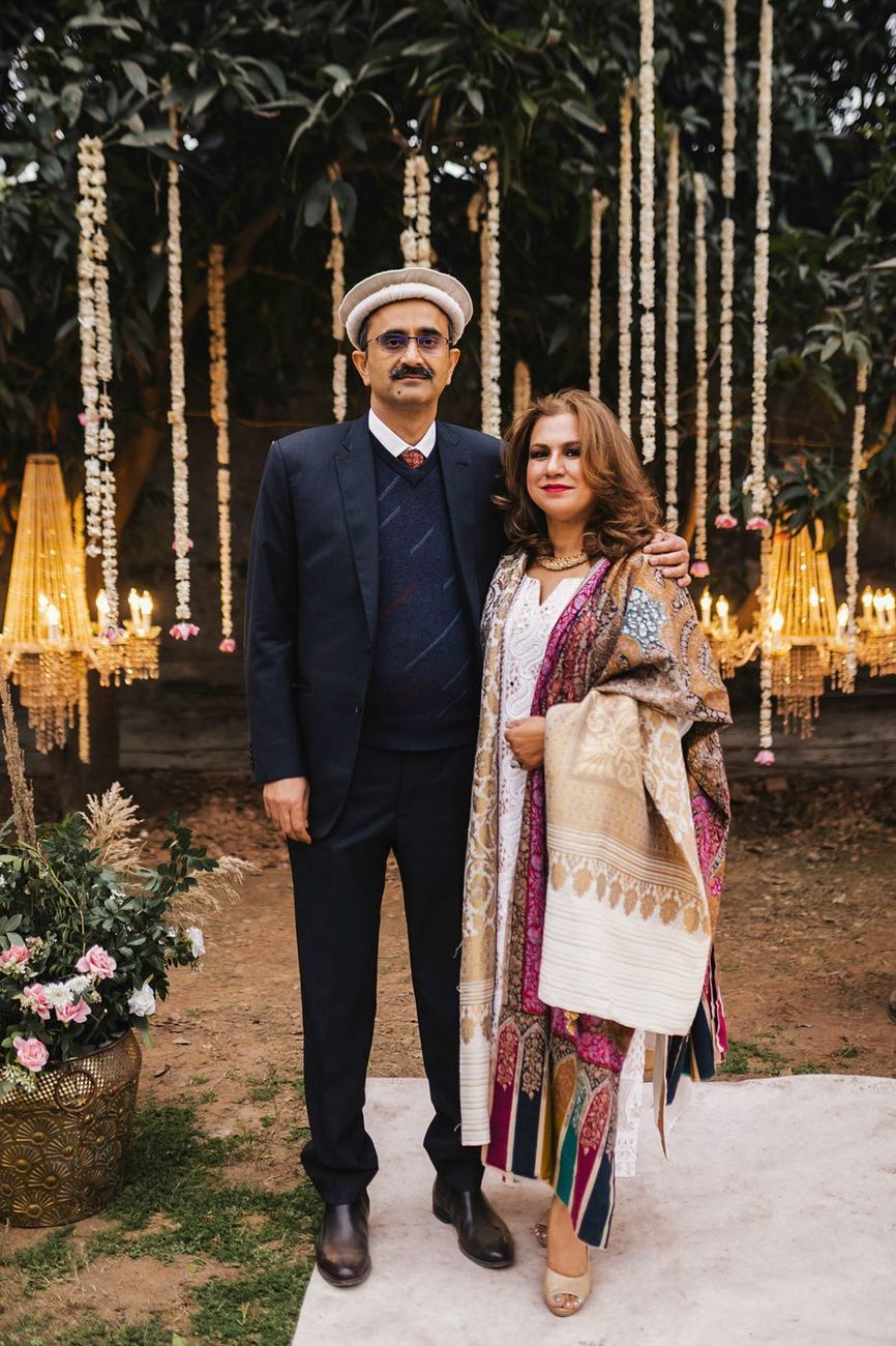 Older couple, the man wearing a traditional cap, posed near the lit chandelier decor
