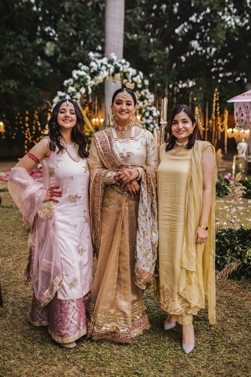 Bride posed standing with two female friends near a decorative floral arch
