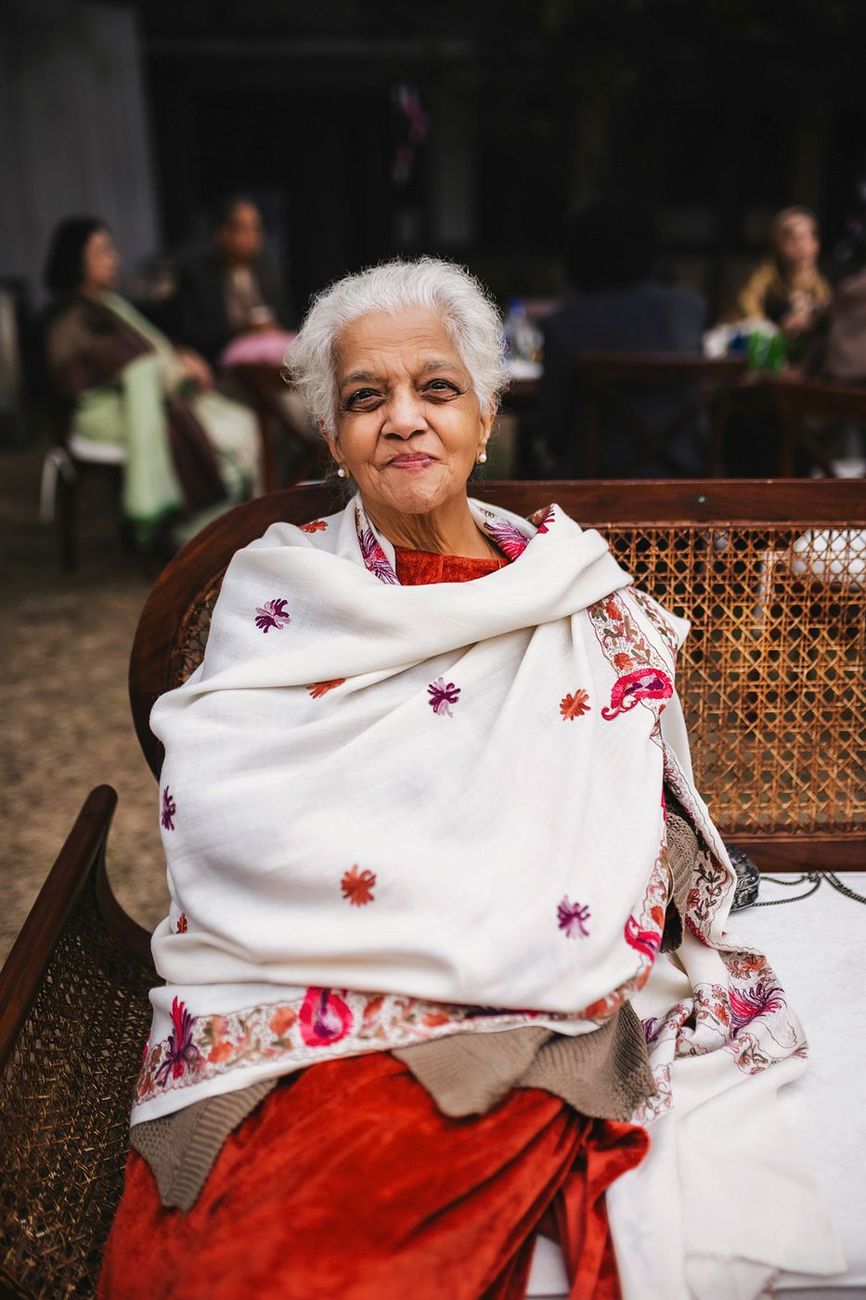Elderly woman seated on a wicker bench, wrapped in an embroidered floral shawl