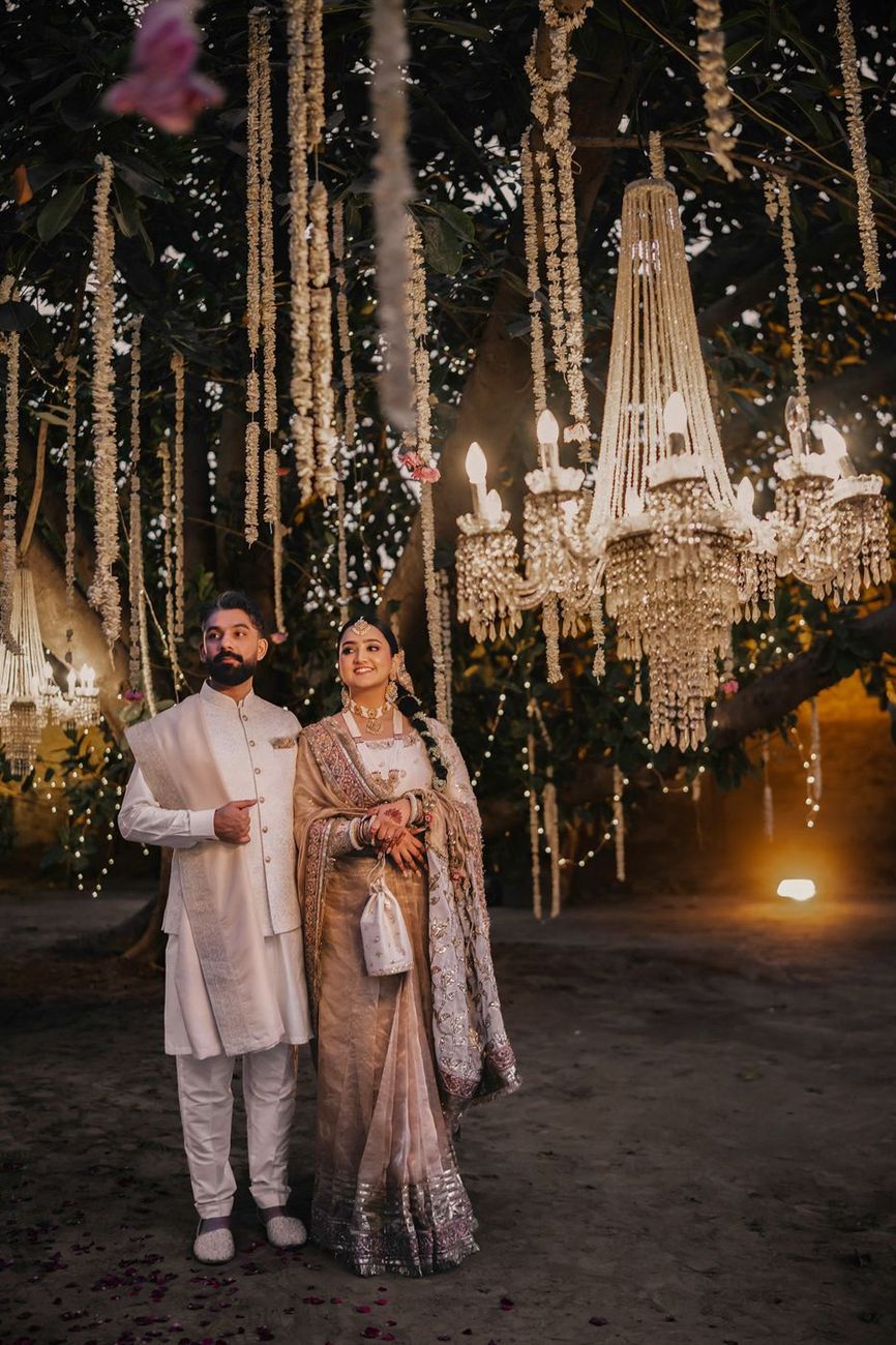 Couple standing beneath a large crystal chandelier hanging from a tree, fairy lights twinkling around them
