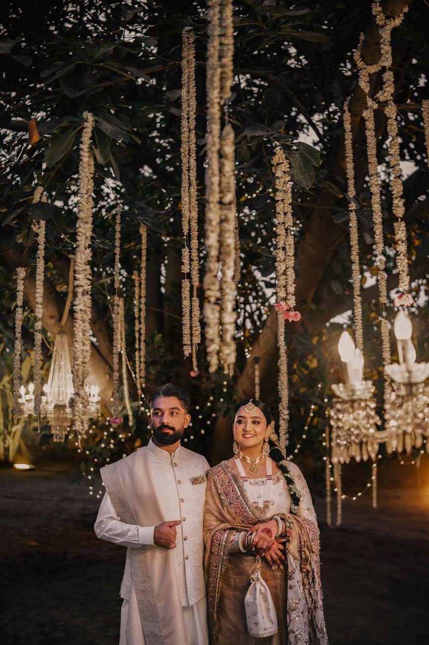 Couple standing beneath cascading garlands and crystal chandeliers, evening light
