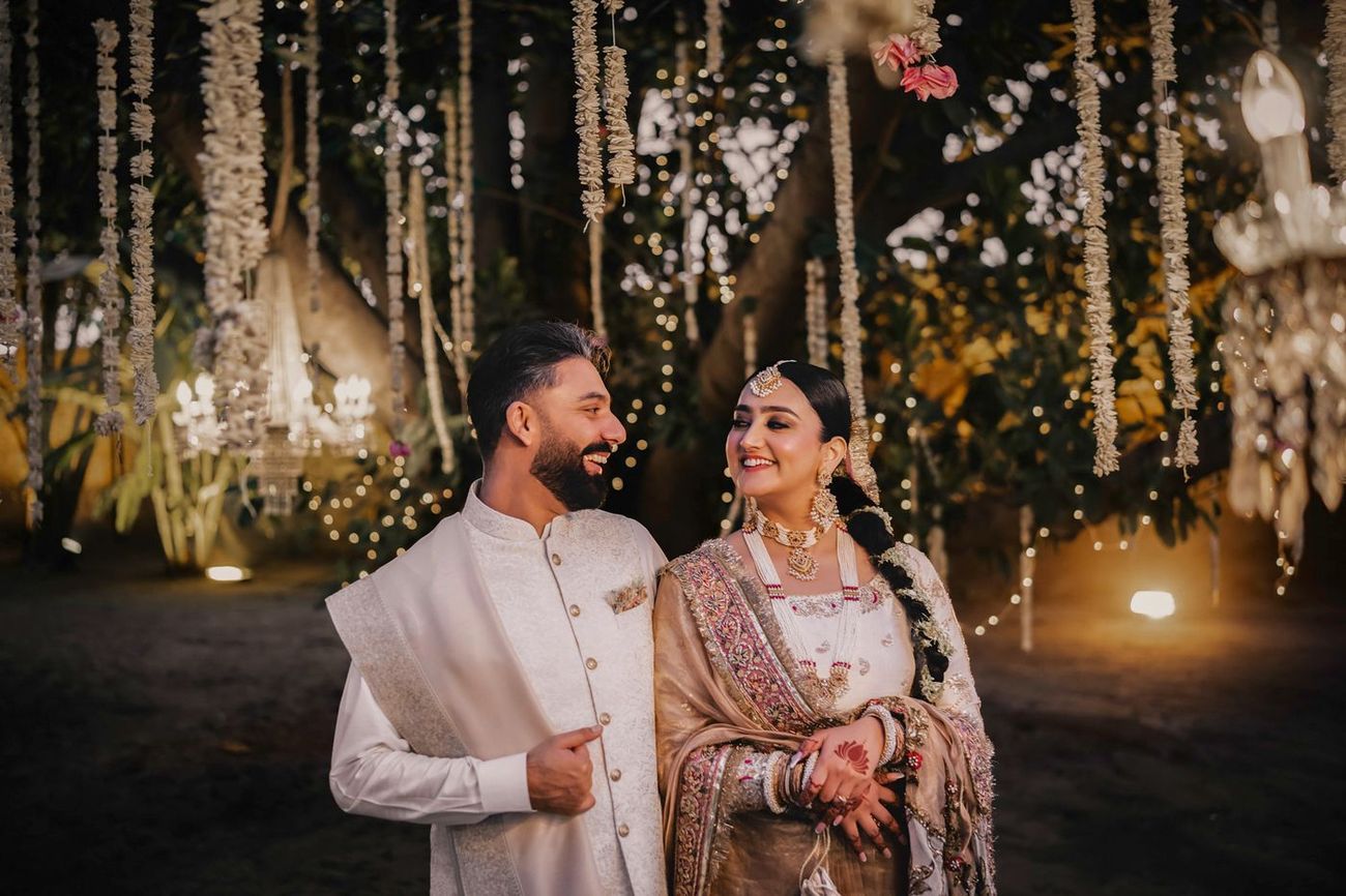 Close evening portrait of the couple smiling at each other under twinkling lights and garlands