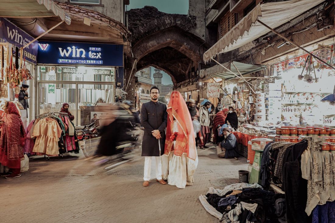 Bride and groom standing together in a bustling old city bazaar street, surrounded by shopfronts and passersby