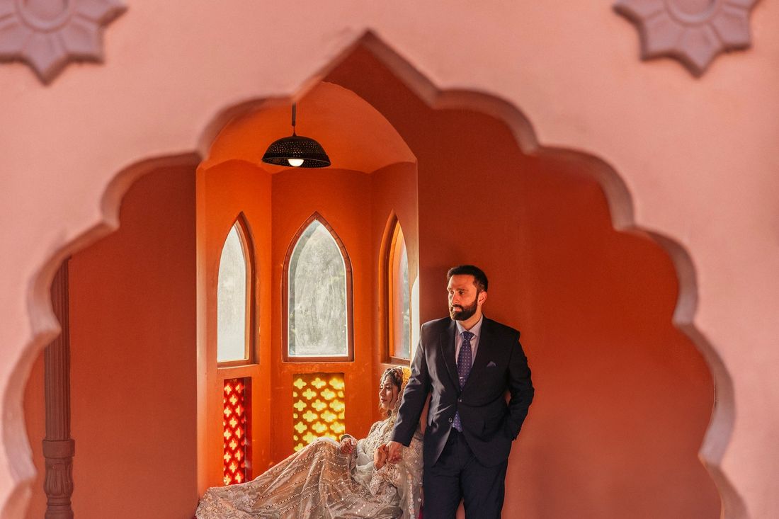 Bride and groom framed within an ornate scalloped archway against a terracotta-colored alcove