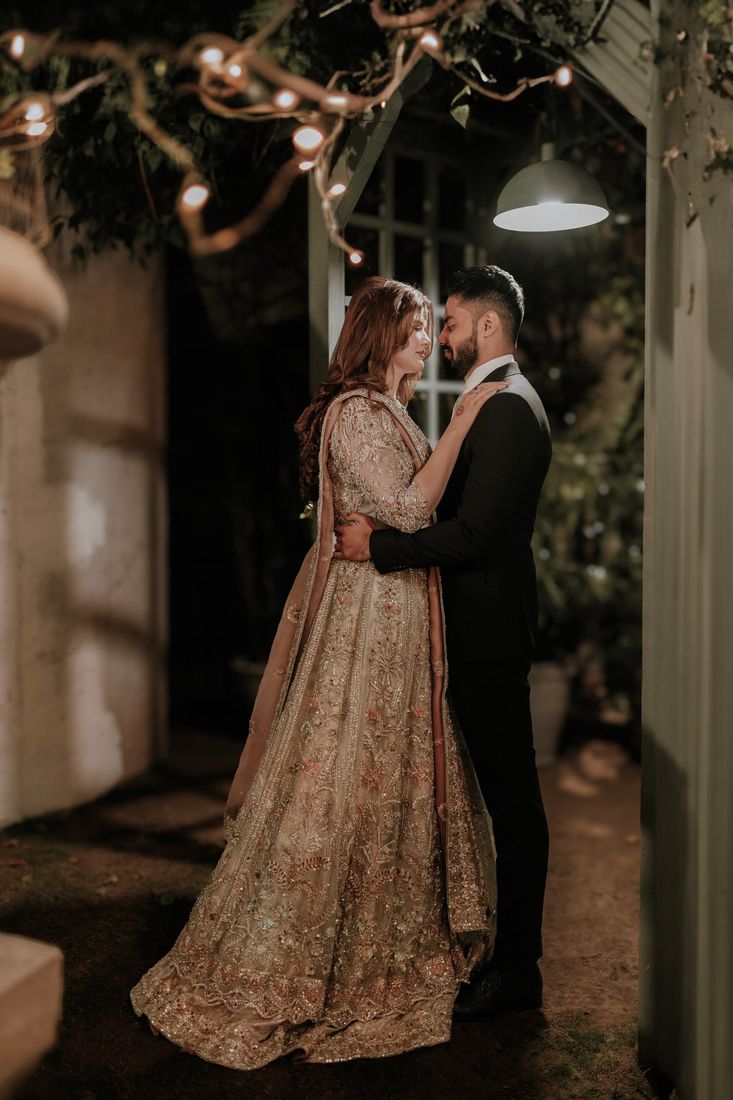 Bride and groom embracing under string lights in a garden doorway at night