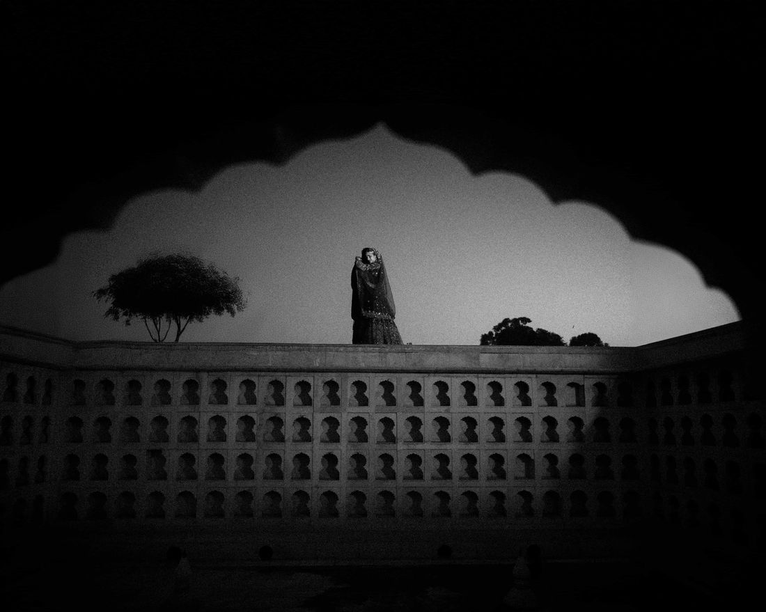 Black-and-white silhouette of a bride standing atop a wall above a honeycomb-patterned heritage facade