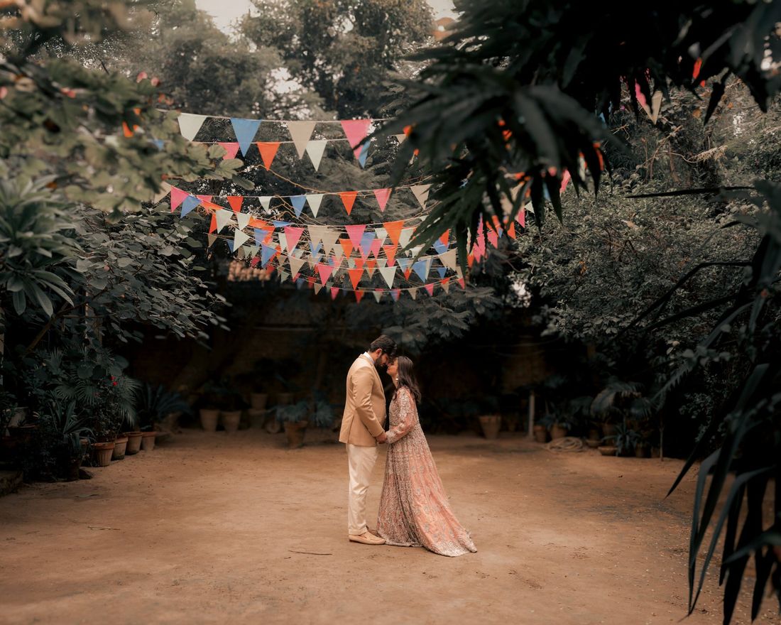 Bride and groom standing close together in a garden courtyard strung with colorful bunting flags