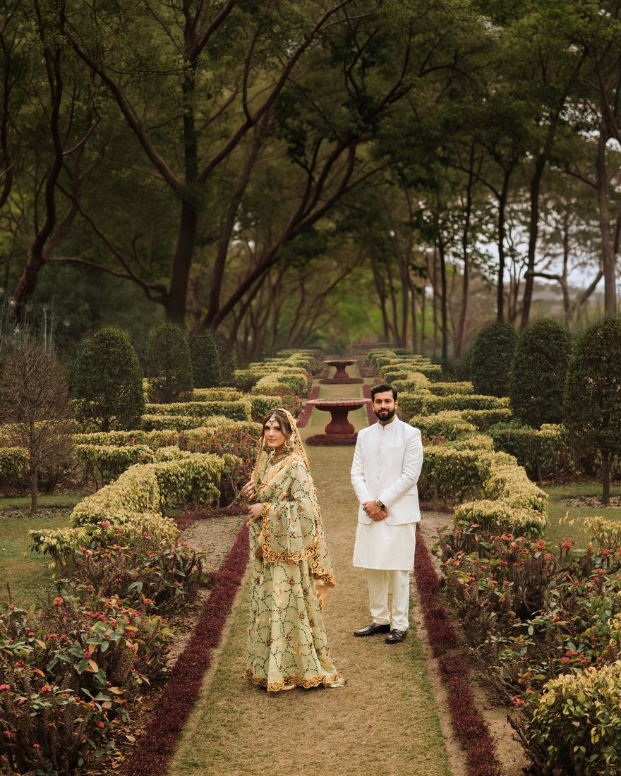Bride and groom standing in a manicured formal garden with symmetrical hedges and a tree-lined path