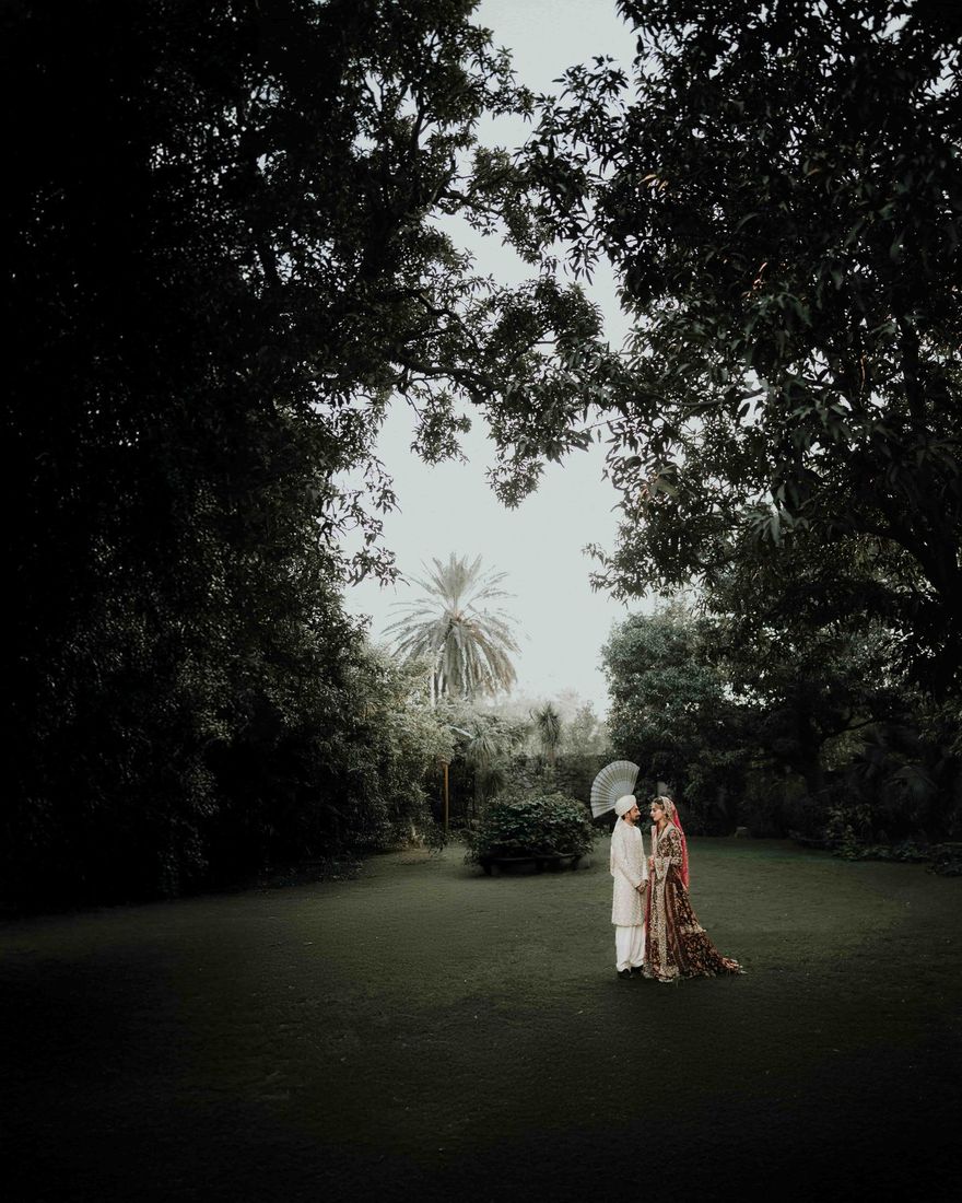Bride and groom standing together in a moody, tree-framed garden clearing at dusk
