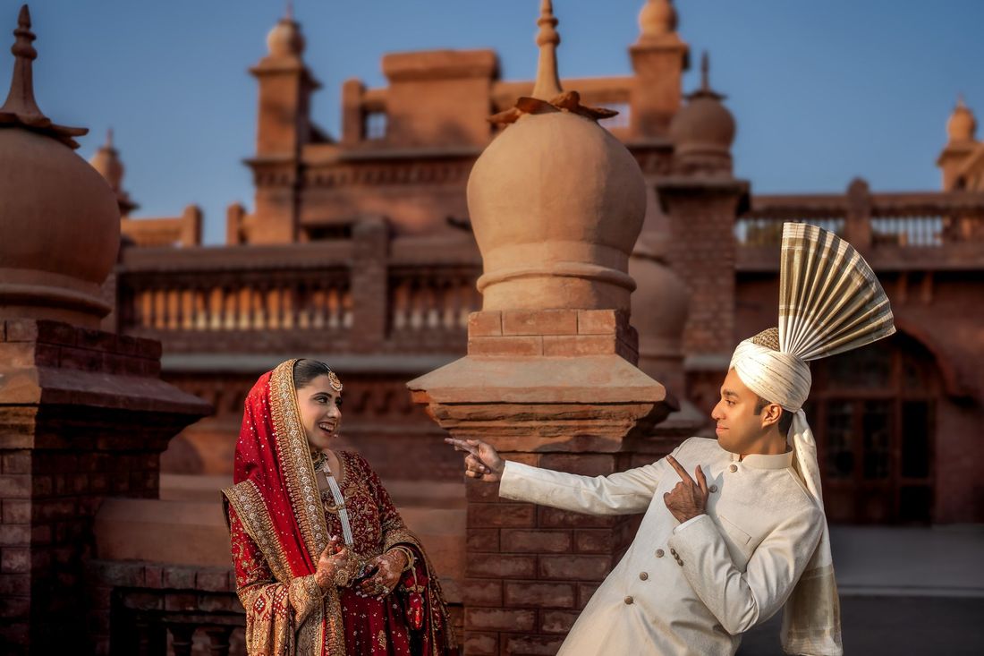 Groom playfully pointing and dancing as the bride laughs, rooftop setting with domed brick finials in the background