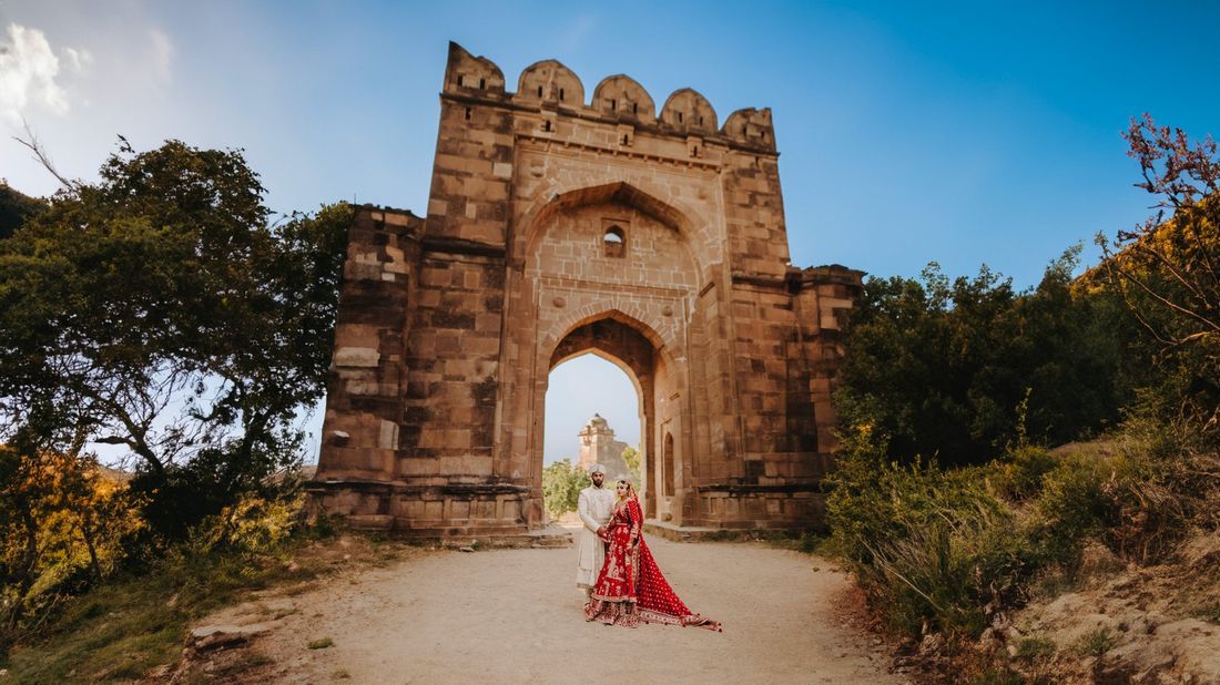 Bride and groom standing before a monumental stone fort gateway with domed parapets