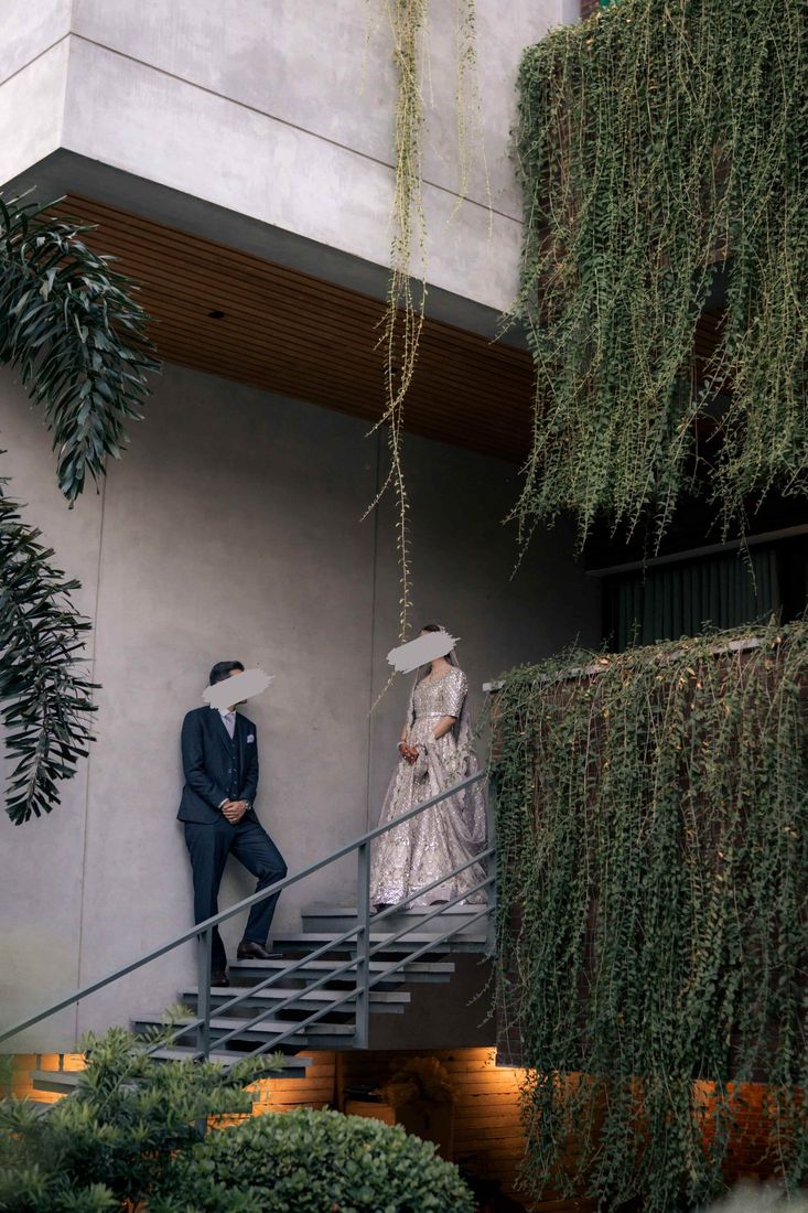 Bride and groom on a modern staircase framed by trailing string-of-pearls vines against a concrete facade