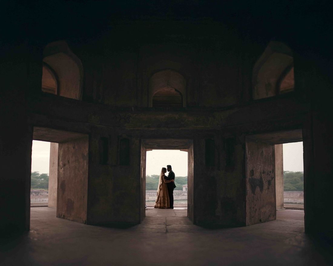 Silhouette of bride and groom embracing in a distant doorway, framed by the multiple archways of a fort tower interior