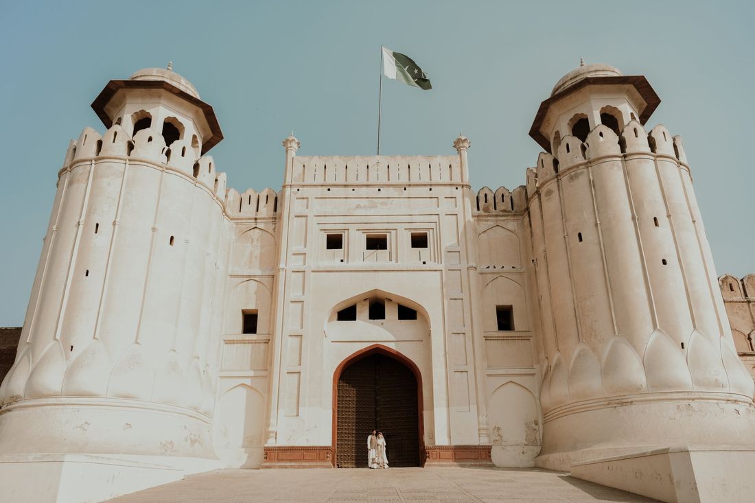 Bride and groom standing before the towering Alamgiri Gate of Lahore Fort, with the Pakistani flag flying above