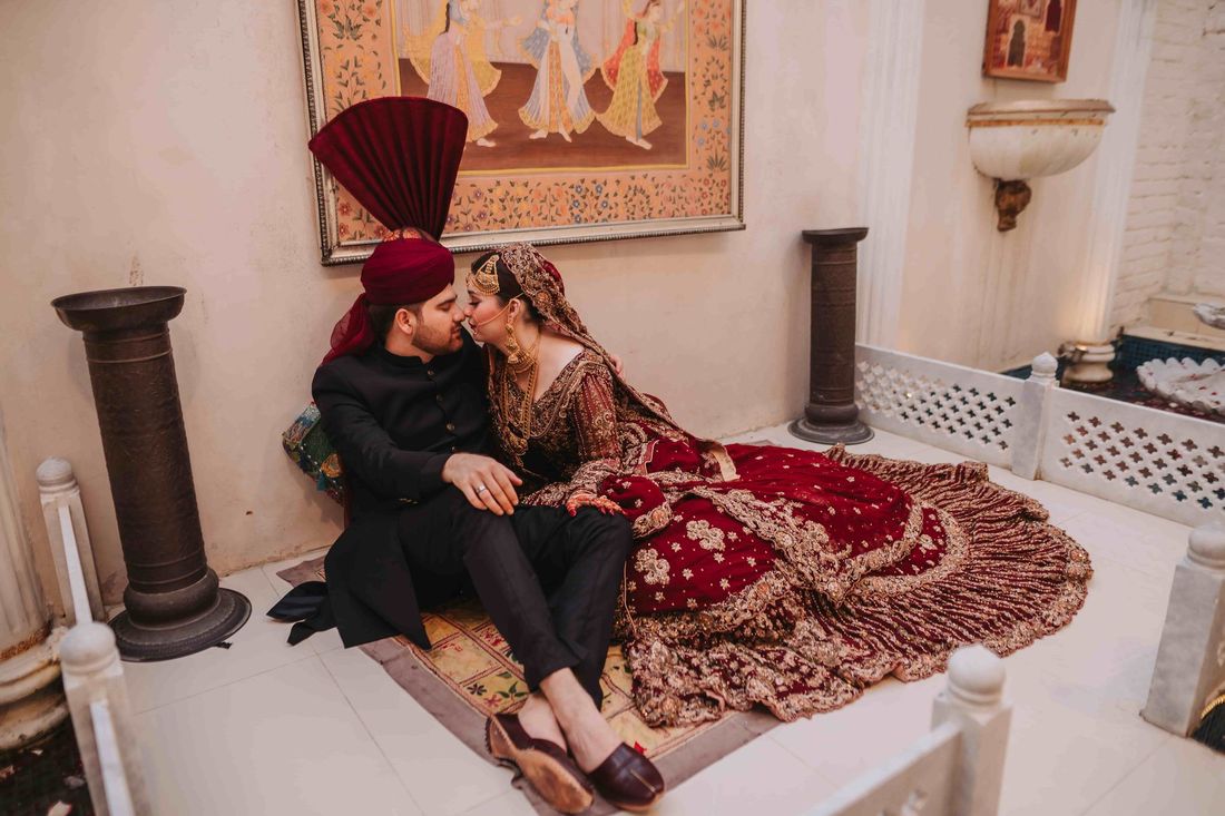 Bride and groom reclining together intimately on a daybed, framed by a Mughal-style miniature painting on the wall behind them