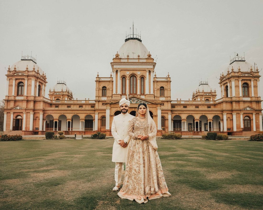 Bride and groom standing on the lawn before the grand domed facade of Noor Mahal, Bahawalpur