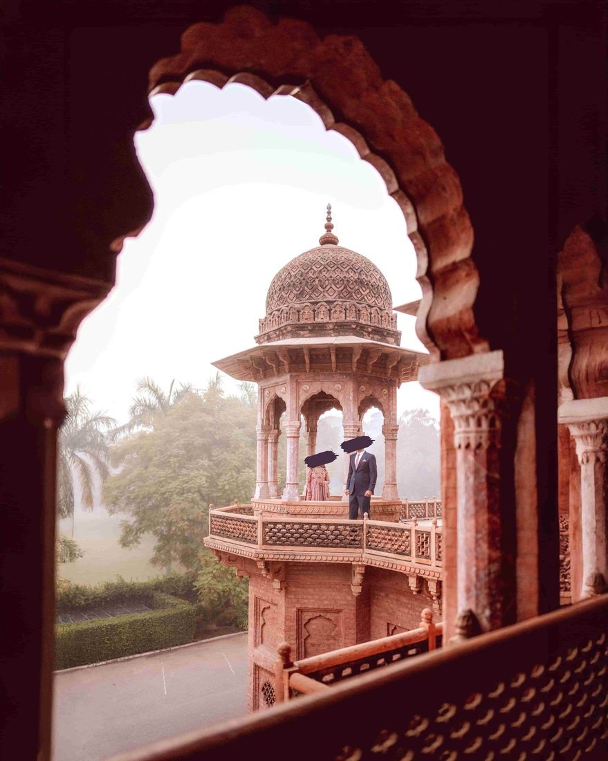 Bride and groom standing on an ornate domed turret balcony, viewed through a scalloped archway