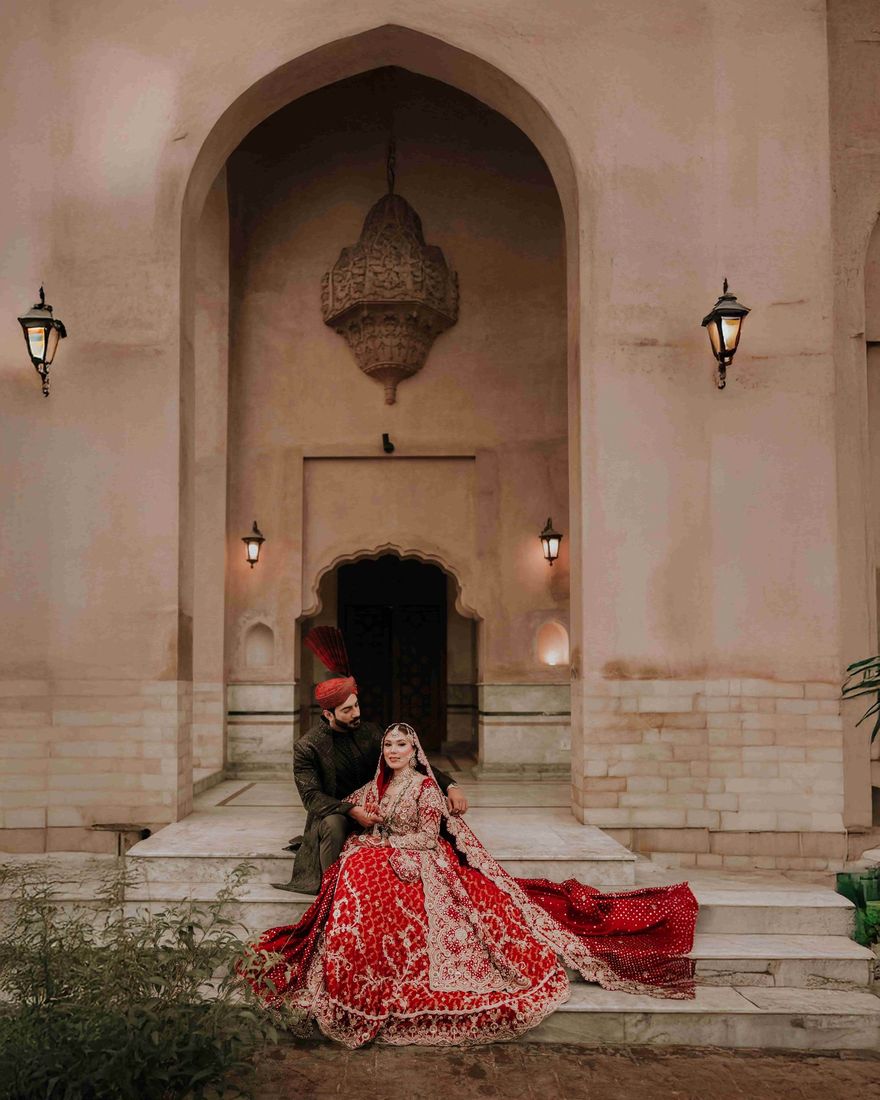 Bride and groom seated on steps before a grand arched doorway with an ornate hanging lantern and wall sconces