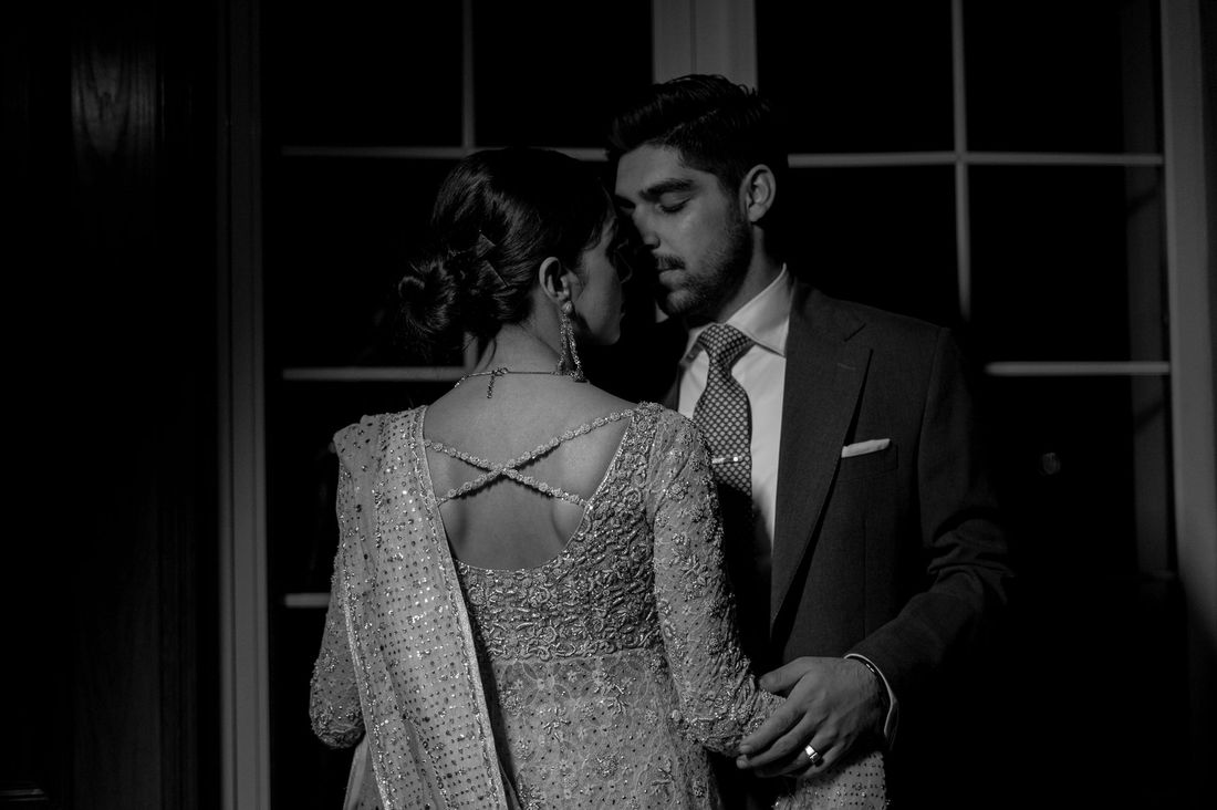 Black-and-white close-up of the bride's embellished open-back blouse as the groom embraces her tenderly