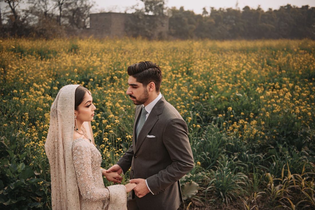 Bride and groom holding hands closely amid a vast mustard flower field