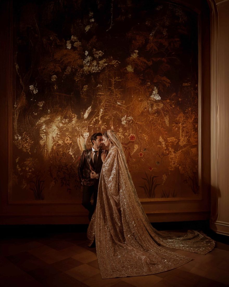 Bride and groom in an intimate moment before a large antique floral mural, dim golden lighting