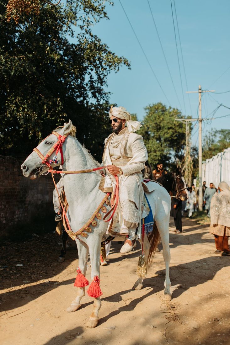 Groom riding a decorated white horse with red tassels during the baraat procession