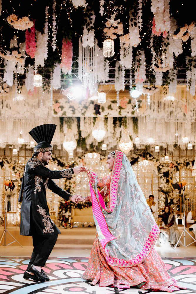 Bride and groom dancing together on the reception floor beneath hanging chandeliers and florals, Zara & Shuaib's wedding at Garrison Halls, Lahore